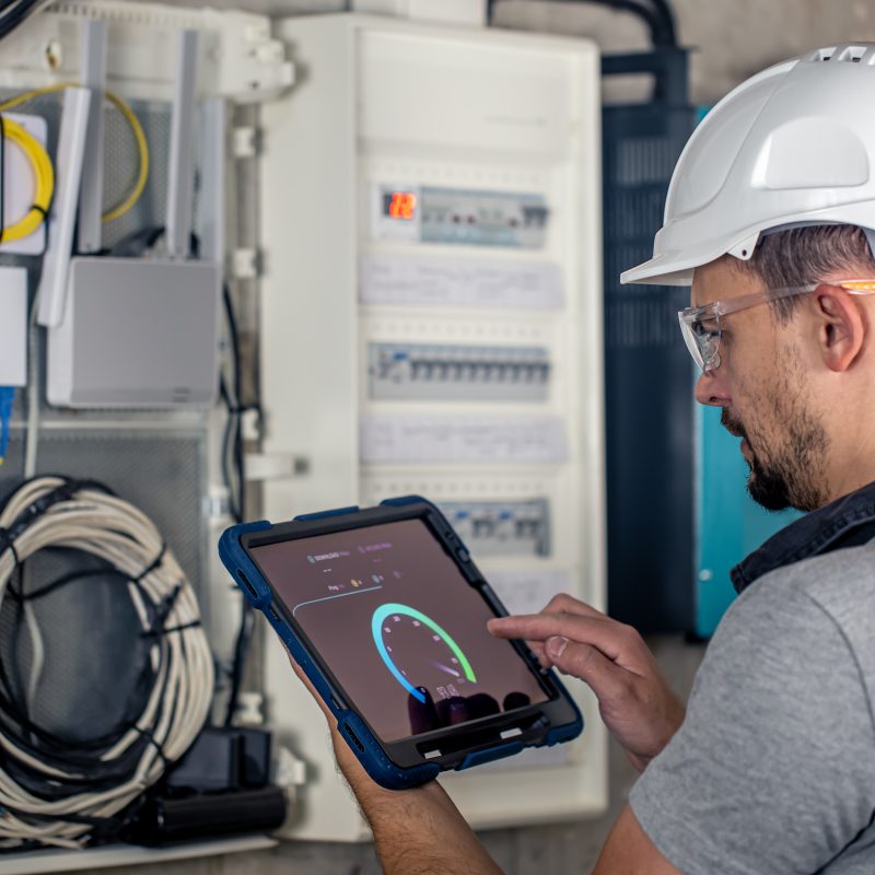 Man, an electrical technician working in a switchboard with fuses, uses a tablet. Man, an electrical technician working in a switchboard with fuses. Installation and connection of electrical equipment.